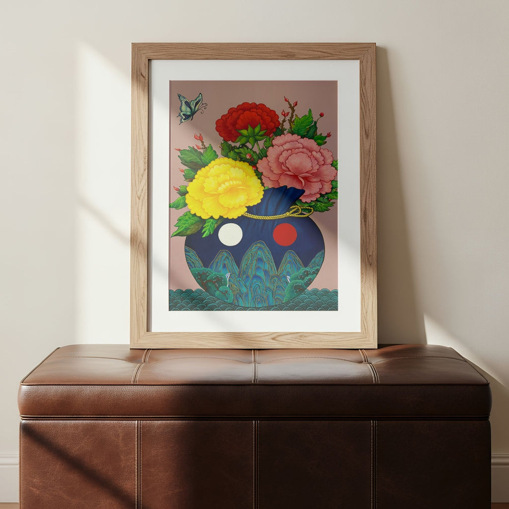 Art print of a bokjumeoni adorned with traditional motifs inspired by Minhwa art holding a bouquet of colorful peonies with a butterfly floating in the corner, representing good fortune, harmony and joy, on a wall above a brown leather bench.