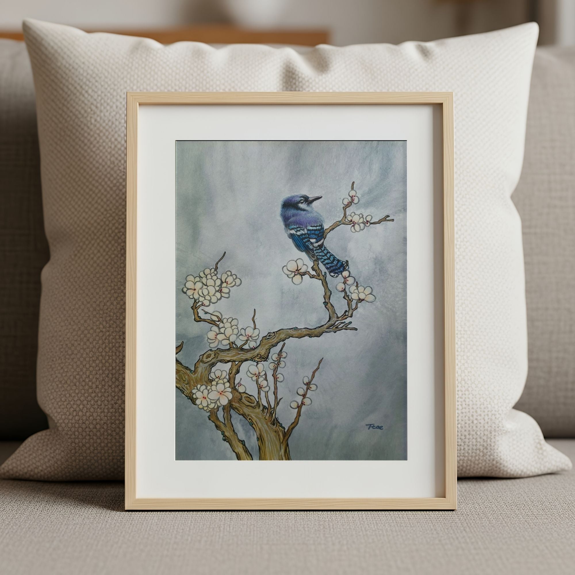 Framed art print of a blue bird on a branch with flowers, placed on a surface, symbolizing freedom and prosperity.