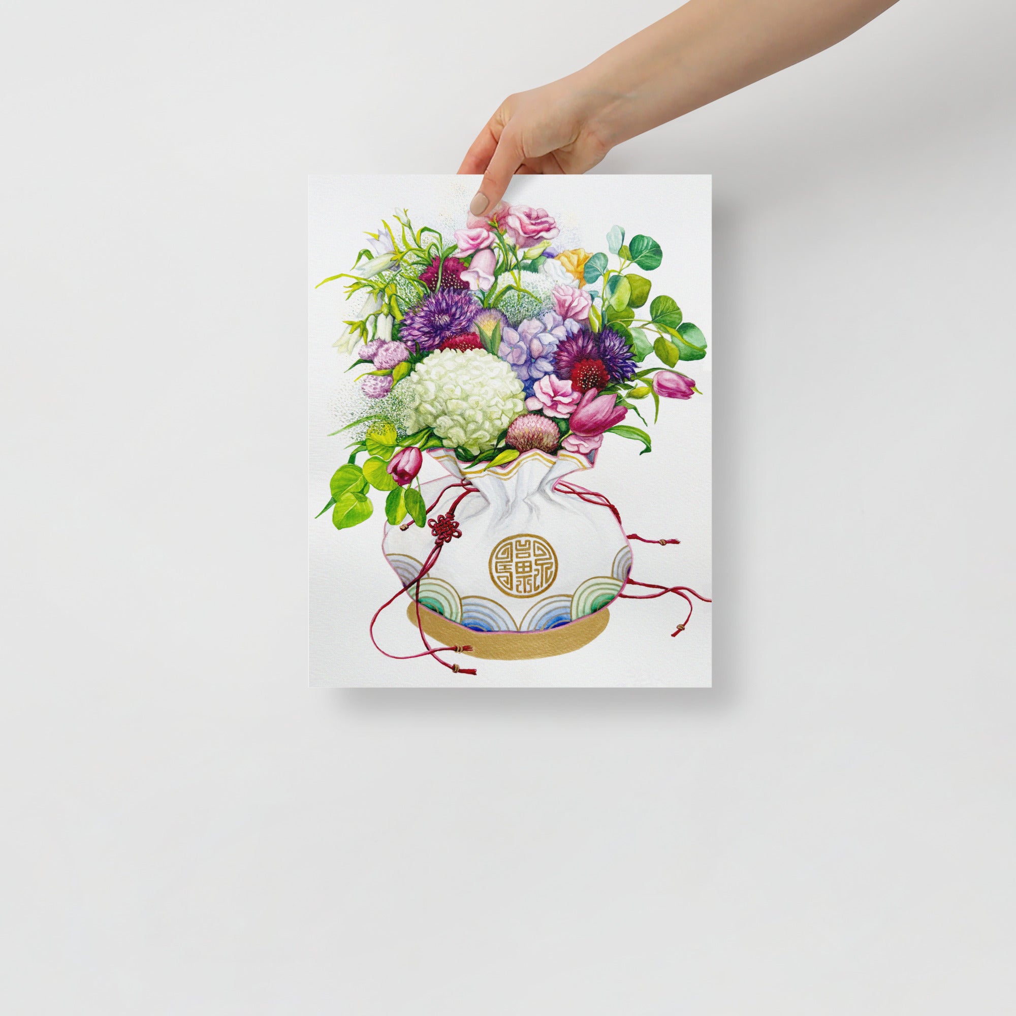 Hand holding a 11x14 inch art print of a Korean coin pouch with a bouquet of flowers, which symbolizes celebrates luck, good health, and fortune.