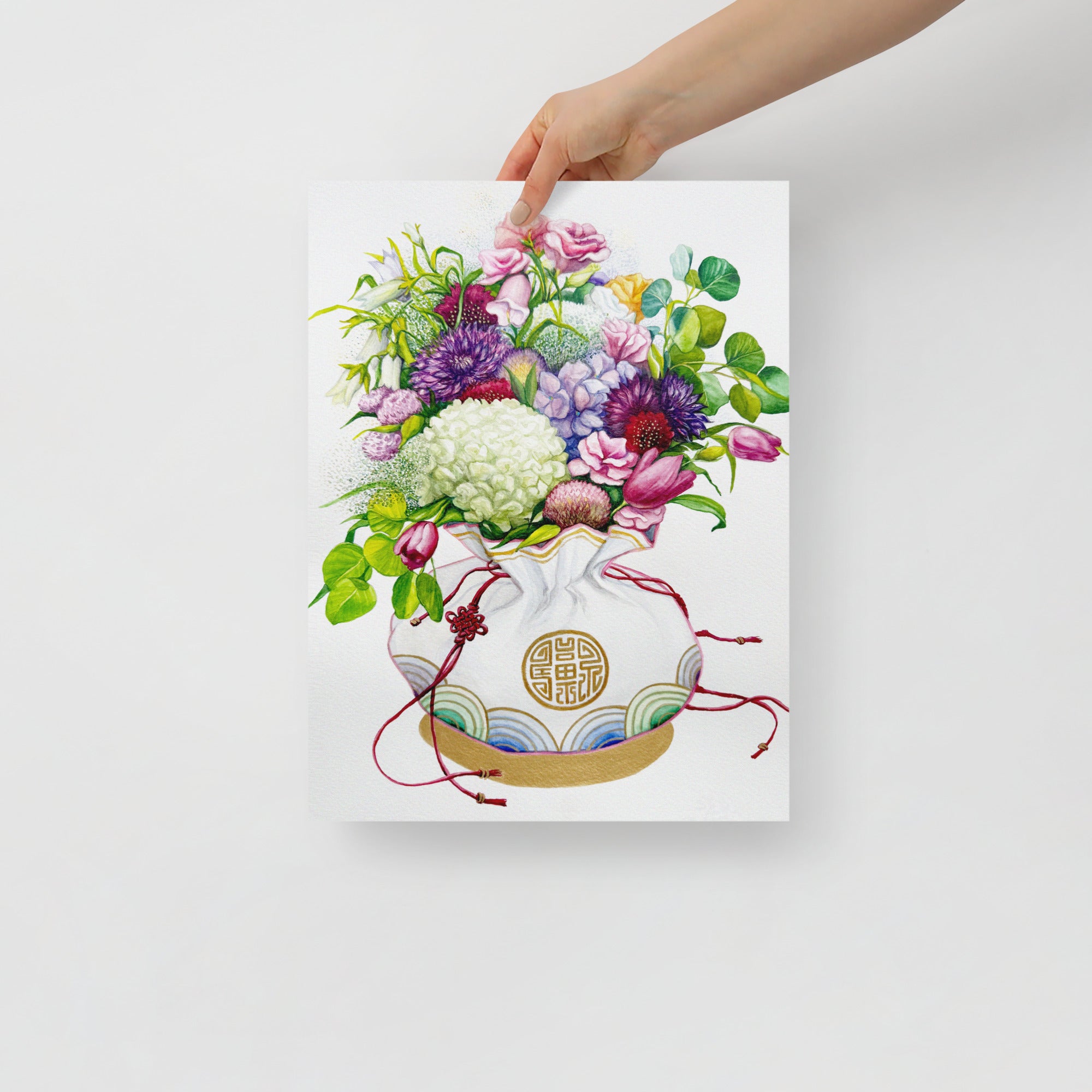 Hand holding a 12x16 inch art print of a Korean coin pouch with a bouquet of flowers, which symbolizes celebrates luck, good health, and fortune.