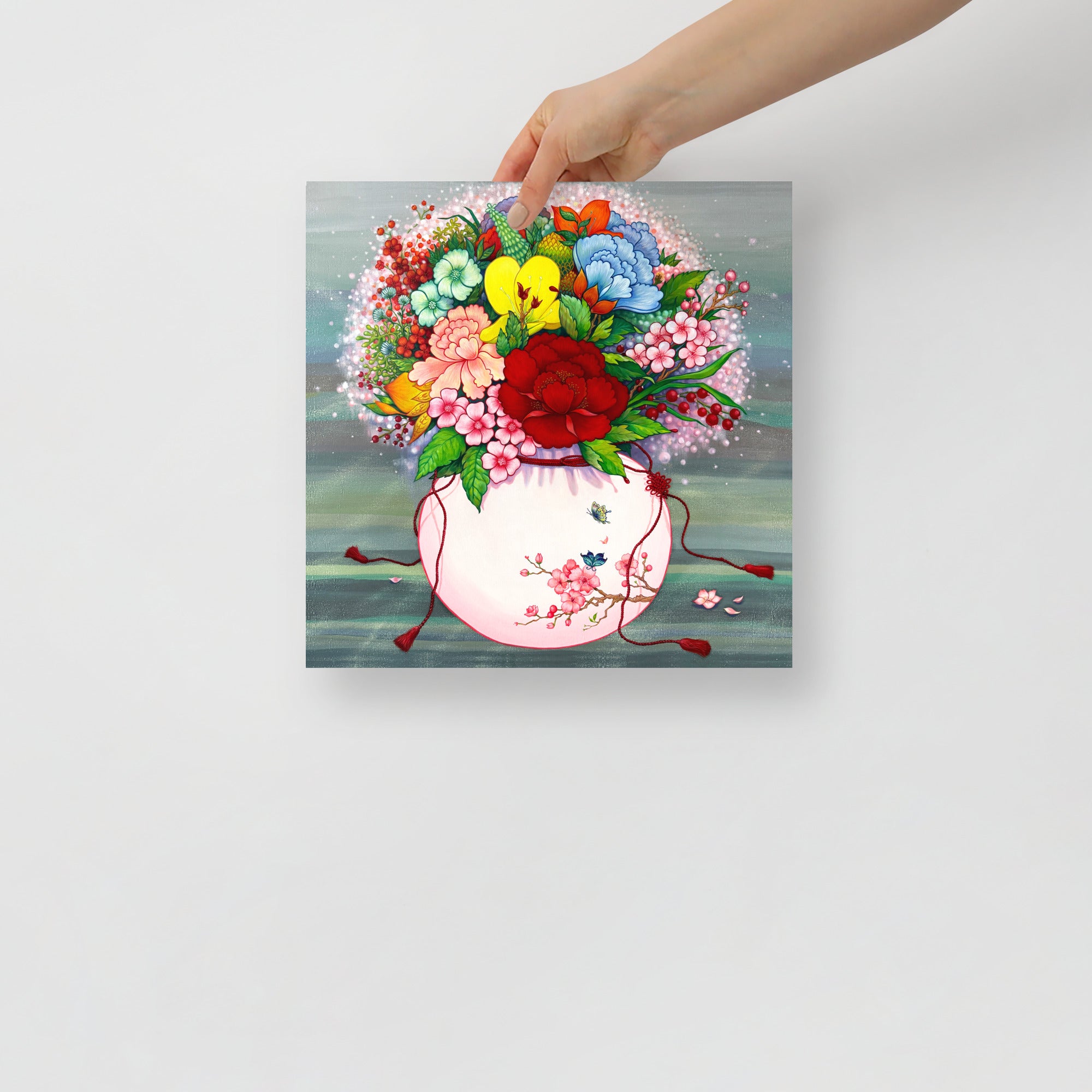 Hand holding a 12x12 inch art print that draws from Korean folk art heritage, weaving together blossoms and traditional motifs that celebrate harmony, wellness, and good fortune.