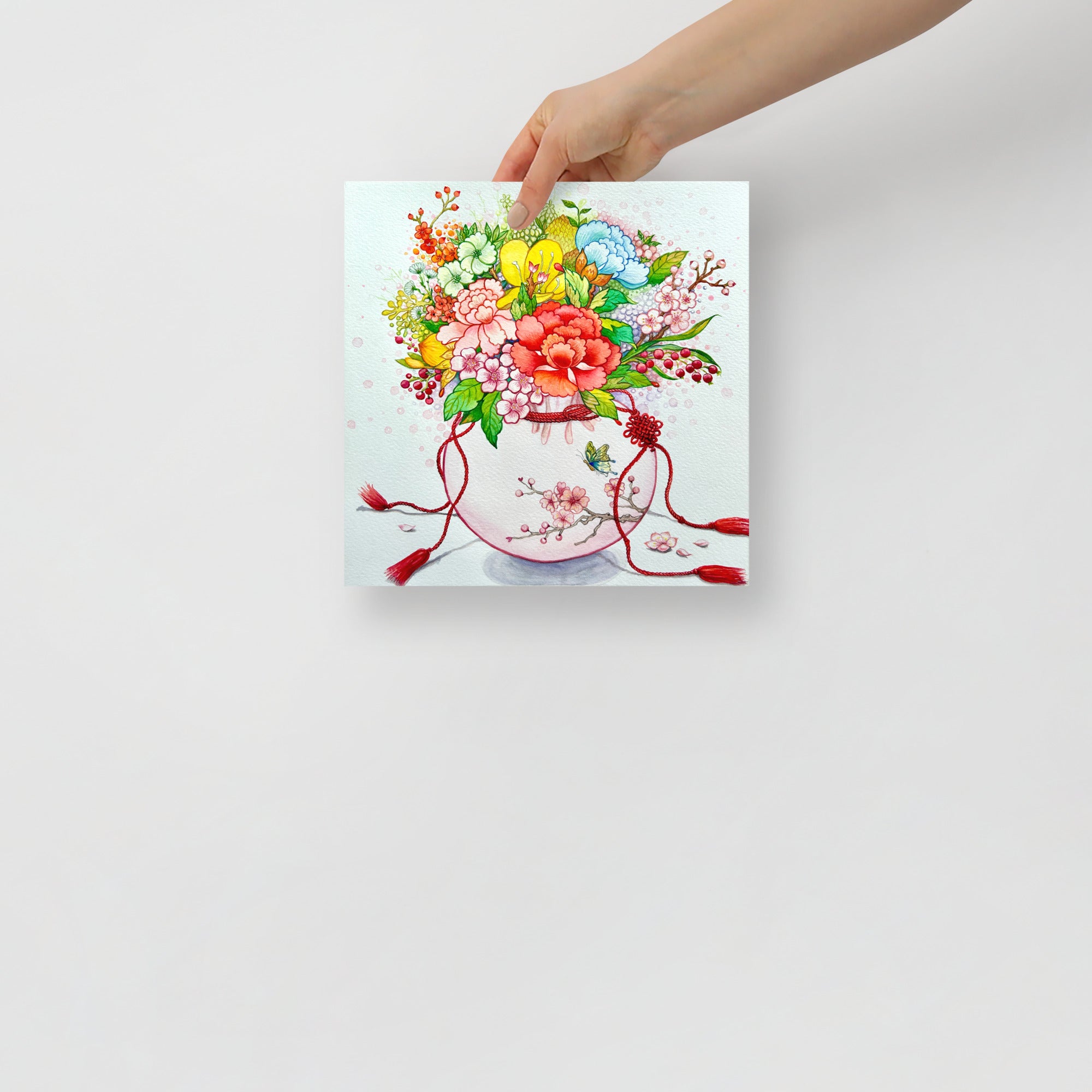 Hand holding an art print with a colorful floral design inspired by Korean folk art on a white background (10x10 size).